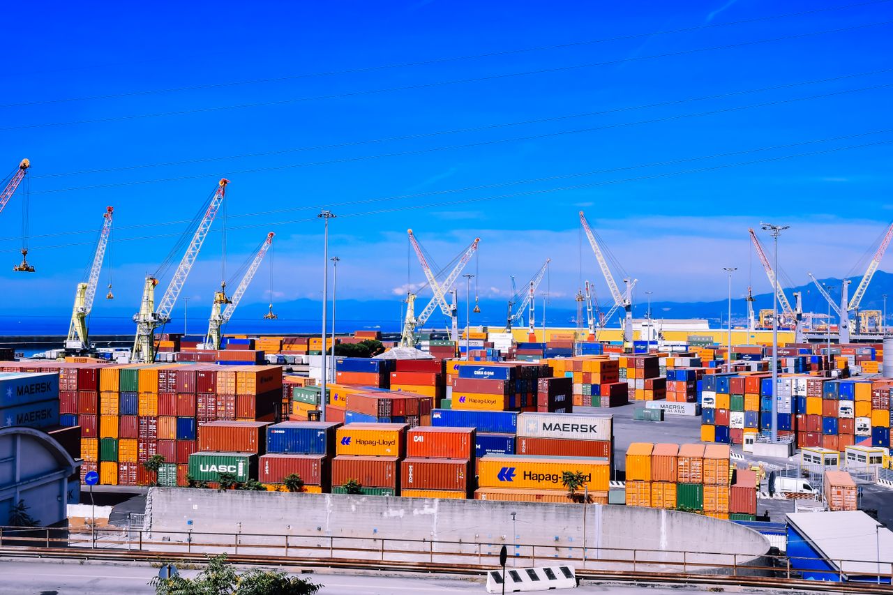 A bustling shipping port with colorful stacked containers and numerous cranes under a clear blue sky.