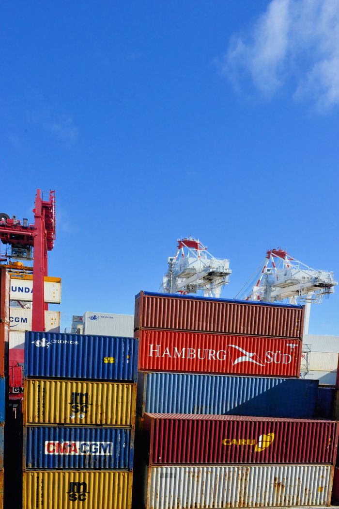 Colorful cargo containers stacked at a busy shipping port under a clear blue sky.