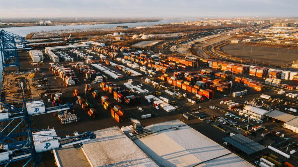 Drone view of industrial district with cargo containers and metal lifting cranes near river of contemporary city