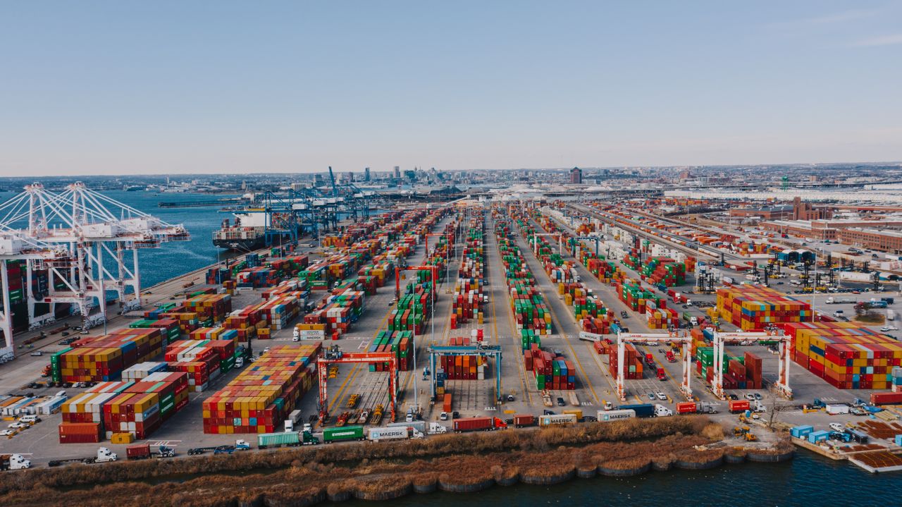 Drone view of river embankment with various bright cargo containers near steel lifting cranes under cloudless sky
